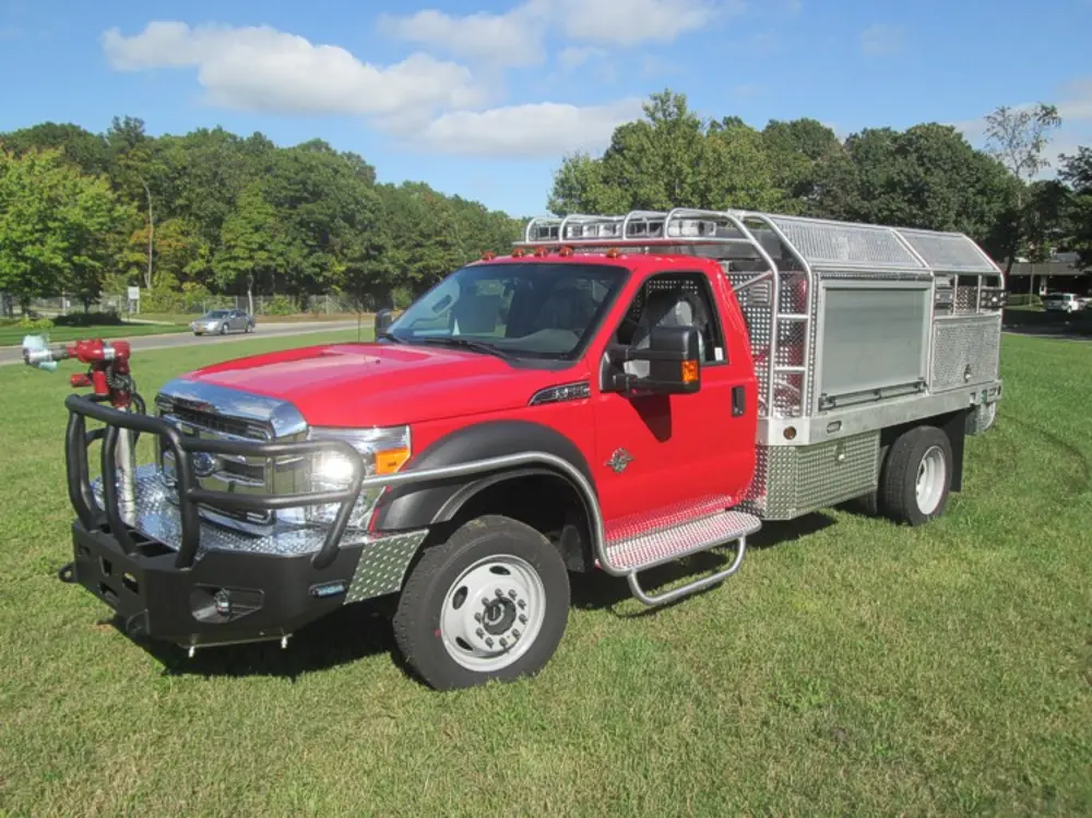 Exterior view of small fire truck showing cab, body compartments, and wheel/tire area.