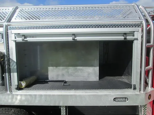 Exterior view of small fire truck showing cab, body compartments, and wheel/tire area.