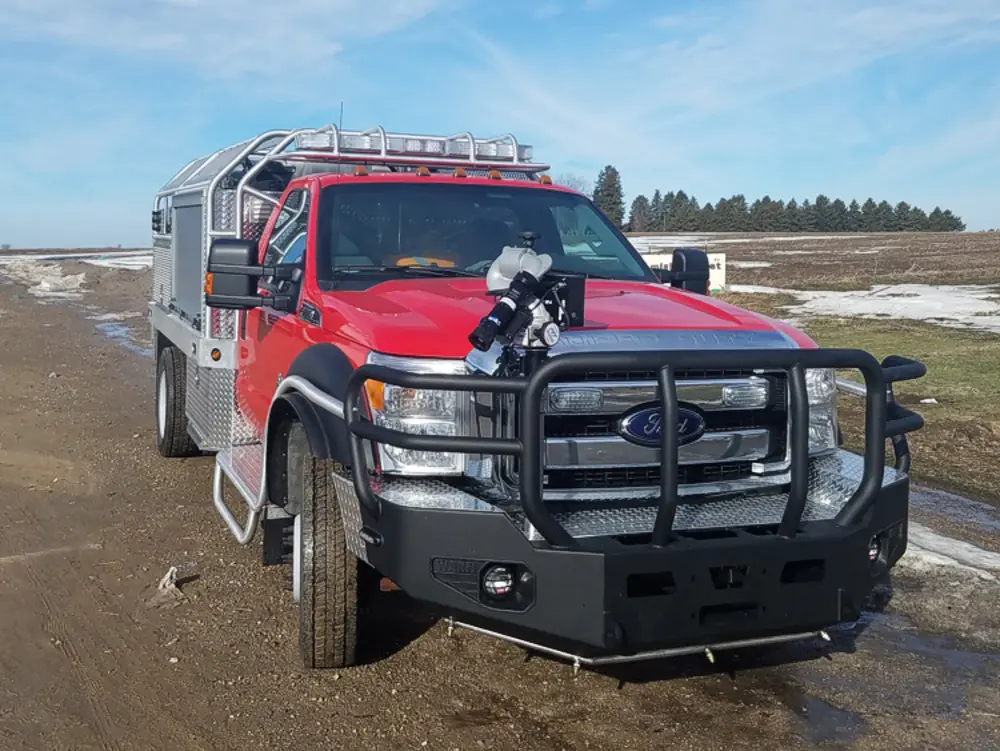 Exterior view of small fire truck showing cab, body compartments, and wheel/tire area.