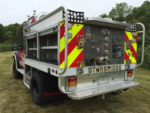 Exterior view of small fire truck showing cab, body compartments, and wheel/tire area.