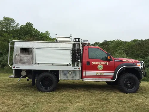 Exterior view of small fire truck showing cab, body compartments, and wheel/tire area.