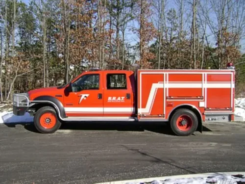 Exterior view of small fire truck showing cab, body compartments, and wheel/tire area.