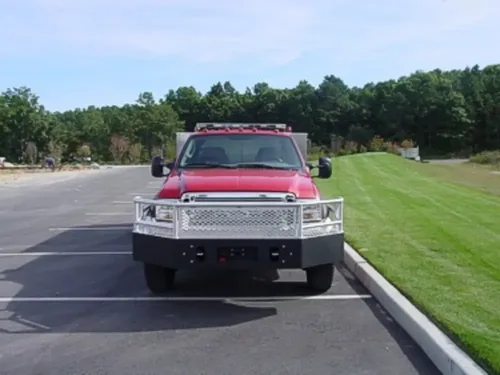 Exterior view of small fire truck showing cab, body compartments, and wheel/tire area.