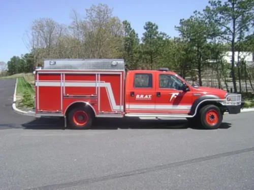 Exterior view of small fire truck showing cab, body compartments, and wheel/tire area.