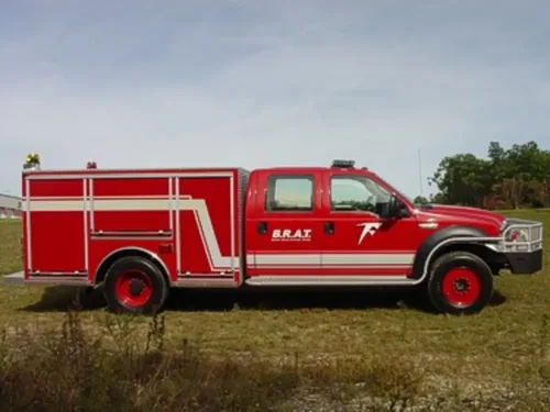 Exterior view of small fire truck showing cab, body compartments, and wheel/tire area.