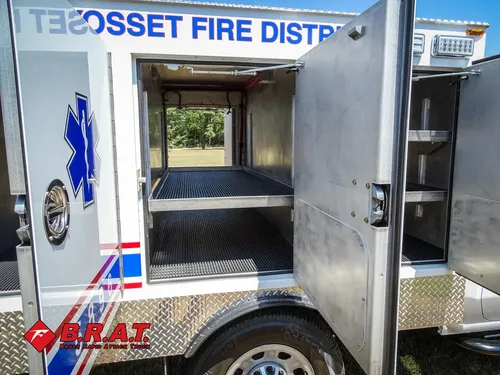 Exterior view of small fire truck showing cab, body compartments, and wheel/tire area.