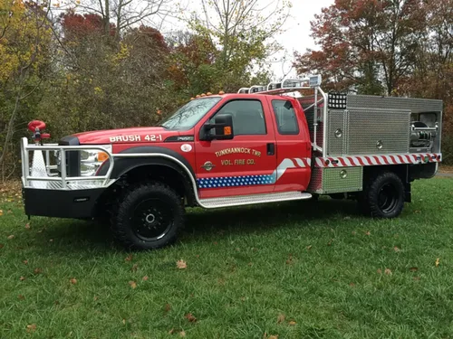 Exterior view of small fire truck showing cab, body compartments, and wheel/tire area.
