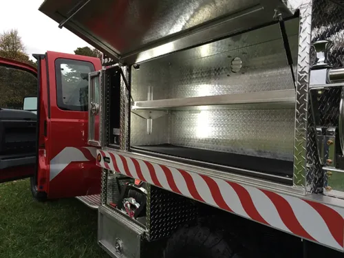 Exterior view of small fire truck showing cab, body compartments, and wheel/tire area.