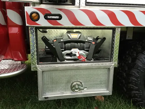 Exterior view of small fire truck showing cab, body compartments, and wheel/tire area.