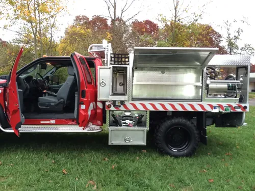 Exterior view of small fire truck showing cab, body compartments, and wheel/tire area.