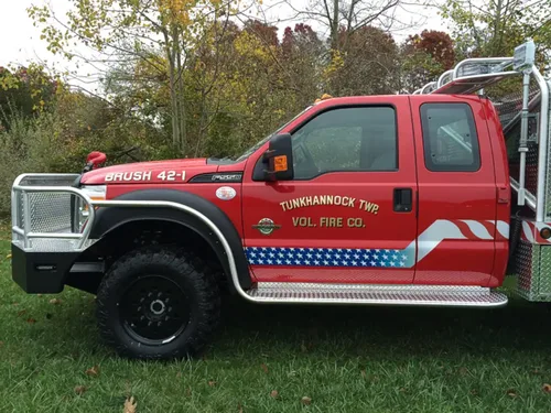 Exterior view of small fire truck showing cab, body compartments, and wheel/tire area.