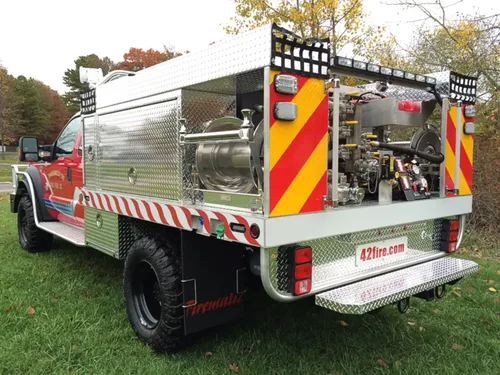 Exterior view of small fire truck showing cab, body compartments, and wheel/tire area.