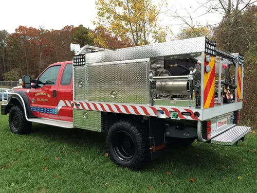Exterior view of small fire truck showing cab, body compartments, and wheel/tire area.
