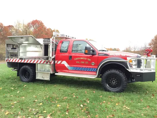 Exterior view of small fire truck showing cab, body compartments, and wheel/tire area.