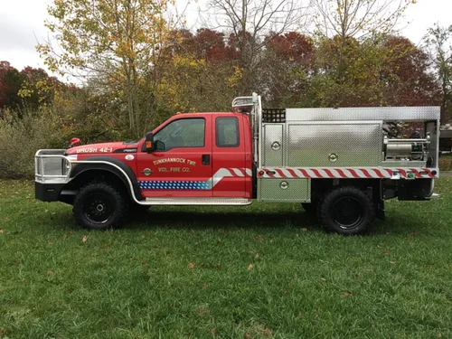 Exterior view of small fire truck showing cab, body compartments, and wheel/tire area.