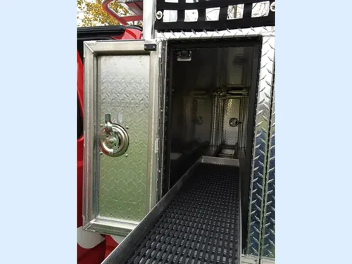 Exterior view of small fire truck showing cab, body compartments, and wheel/tire area.
