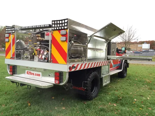Exterior view of small fire truck showing cab, body compartments, and wheel/tire area.