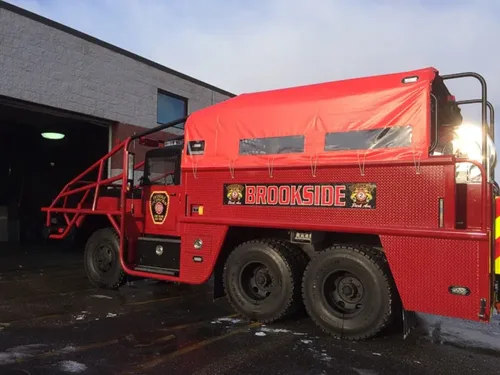 Exterior view of small fire truck showing cab, body compartments, and wheel/tire area.
