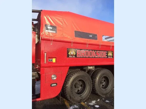 Exterior view of small fire truck showing cab, body compartments, and wheel/tire area.
