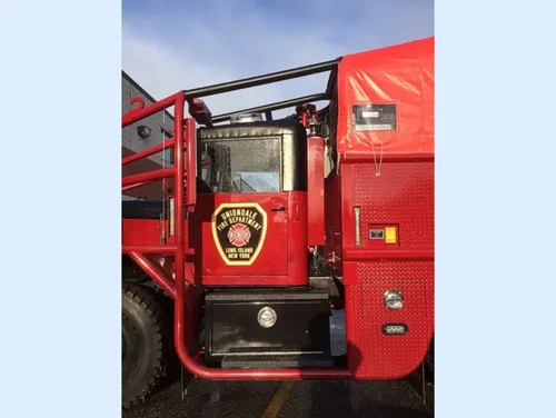 Exterior view of small fire truck showing cab, body compartments, and wheel/tire area.