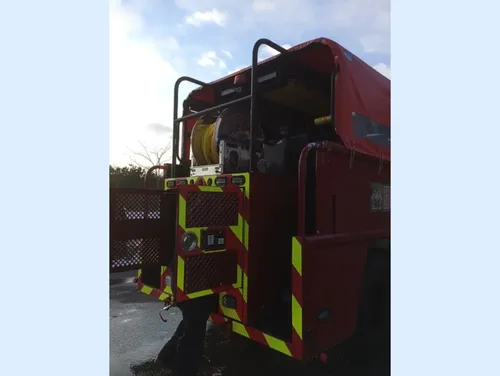 Exterior view of small fire truck showing cab, body compartments, and wheel/tire area.