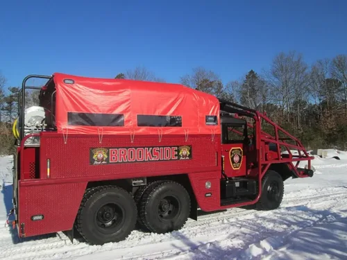 Exterior view of small fire truck showing cab, body compartments, and wheel/tire area.