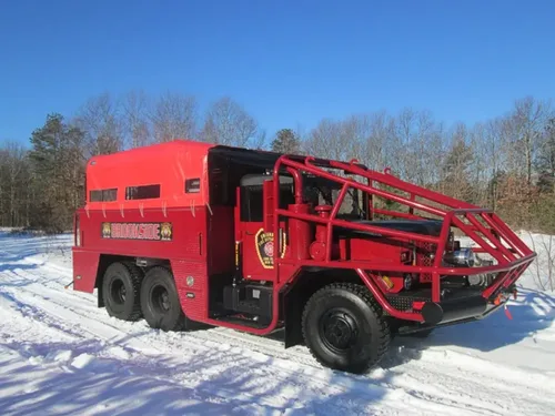 Exterior view of small fire truck showing cab, body compartments, and wheel/tire area.