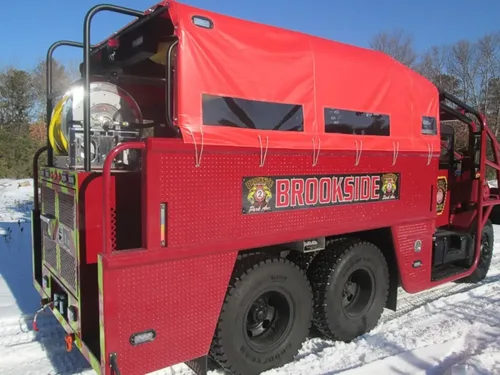 Exterior view of small fire truck showing cab, body compartments, and wheel/tire area.