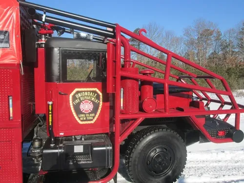 Exterior view of small fire truck showing cab, body compartments, and wheel/tire area.
