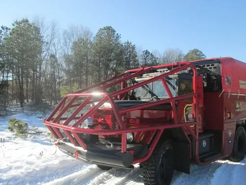 Exterior view of small fire truck showing cab, body compartments, and wheel/tire area.
