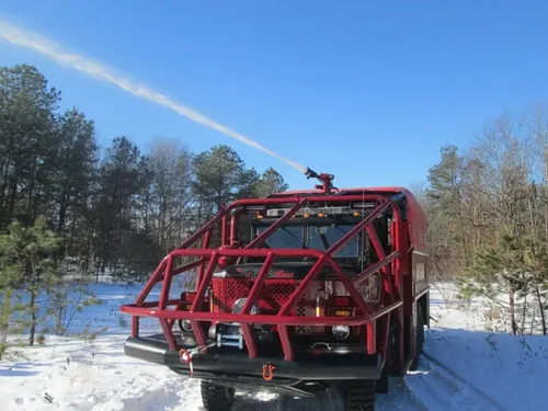 Exterior view of small fire truck showing cab, body compartments, and wheel/tire area.