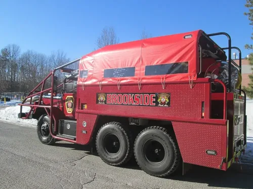 Exterior view of small fire truck showing cab, body compartments, and wheel/tire area.