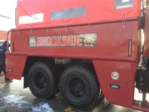 Exterior view of small fire truck showing cab, body compartments, and wheel/tire area.