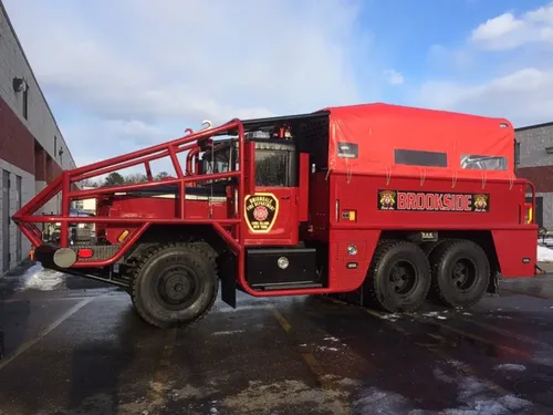 Exterior view of small fire truck showing cab, body compartments, and wheel/tire area.