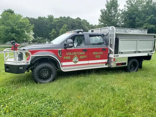 Exterior view of small fire truck showing cab, body compartments, and wheel/tire area.