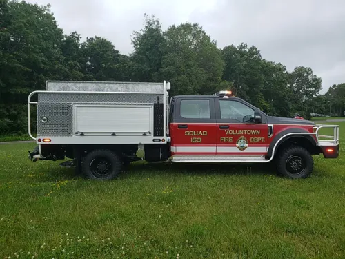 Exterior view of small fire truck showing cab, body compartments, and wheel/tire area.