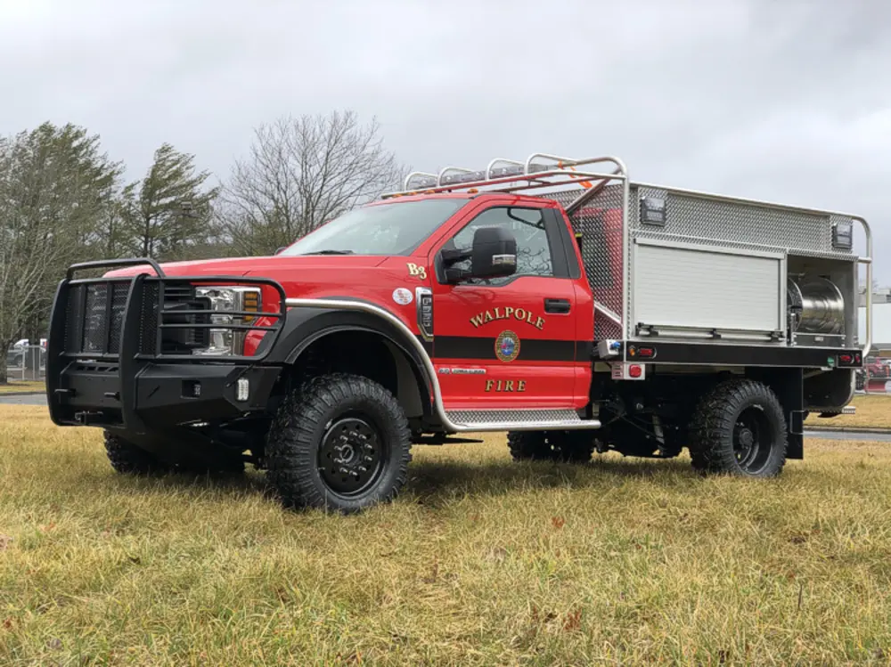 Exterior view of small fire truck showing cab, body compartments, and wheel/tire area.