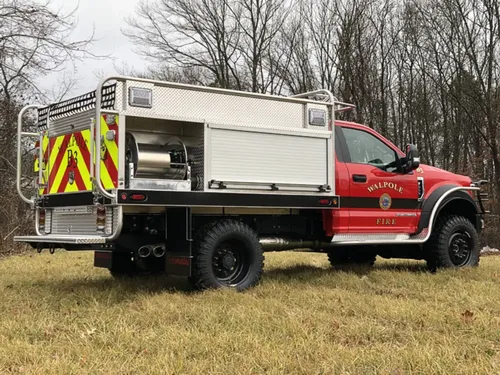 Exterior view of small fire truck showing cab, body compartments, and wheel/tire area.
