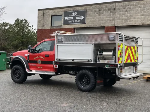 Exterior view of small fire truck showing cab, body compartments, and wheel/tire area.