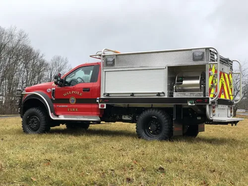 Exterior view of small fire truck showing cab, body compartments, and wheel/tire area.