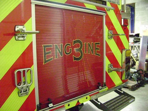 Exterior view of small fire truck showing cab, body compartments, and wheel/tire area.