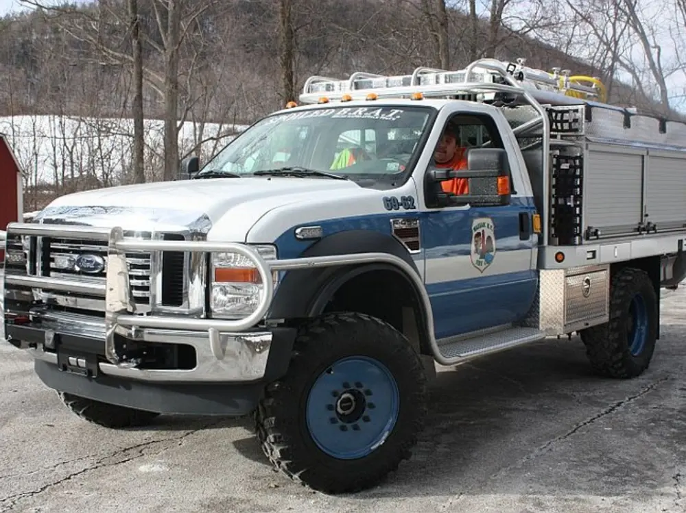 Exterior view of small fire truck showing cab, body compartments, and wheel/tire area.