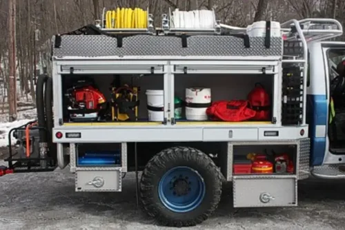 Exterior view of small fire truck showing cab, body compartments, and wheel/tire area.