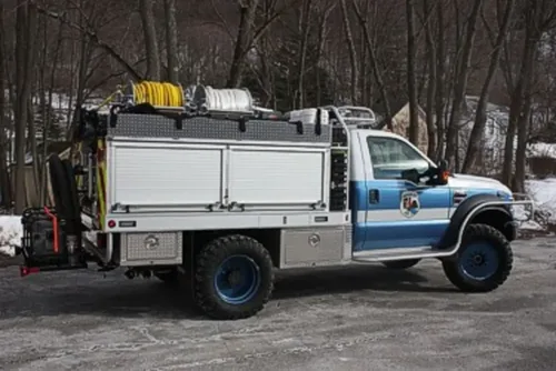 Exterior view of small fire truck showing cab, body compartments, and wheel/tire area.
