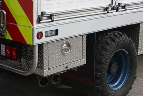 Exterior view of small fire truck showing cab, body compartments, and wheel/tire area.