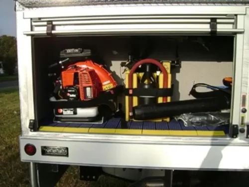 Exterior view of small fire truck showing cab, body compartments, and wheel/tire area.