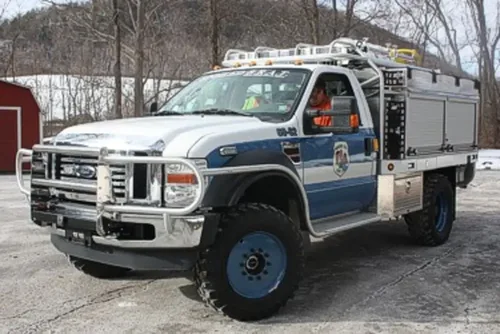 Exterior view of small fire truck showing cab, body compartments, and wheel/tire area.