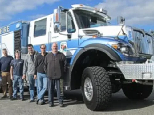 Exterior view of small fire truck showing cab, body compartments, and wheel/tire area.