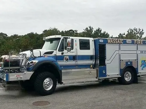 Exterior view of small fire truck showing cab, body compartments, and wheel/tire area.