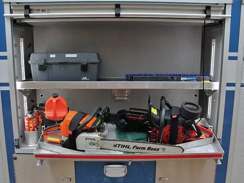 Exterior view of small fire truck showing cab, body compartments, and wheel/tire area.